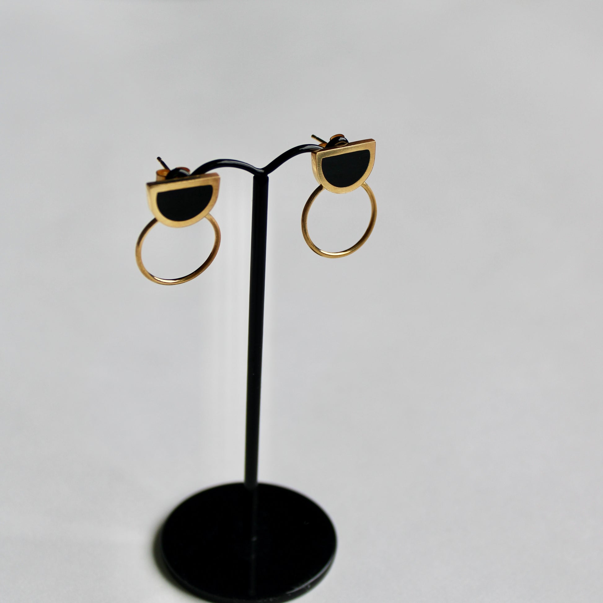 black arc and circle gold earrings on a stand