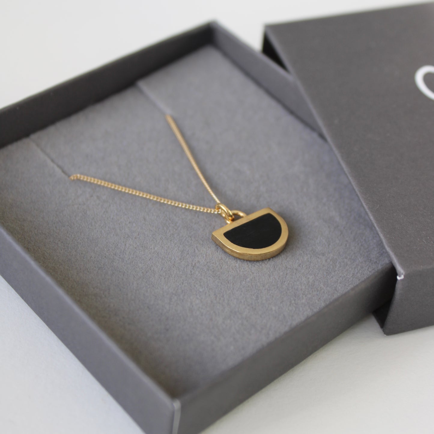 tiny gold arc and black pendant in box
